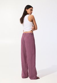 Pantalonii largi cu dungi violet au o talie înaltă și o croială lejeră, asociați cu un top alb ajustat. Țesătura pare netedă.
