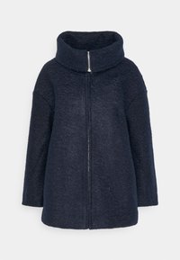 Marinblå ullkappa med hög krage, dragkedjestängning och bred, avslappnad passform. Texturen är mjuk och något fuzzy.