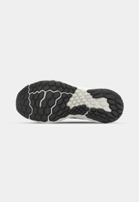 La semelle de chaussure présente un design en caoutchouc noir texturé avec un motif hexagonal, accentué par du blanc et une touche de vert fluo le long des bords.