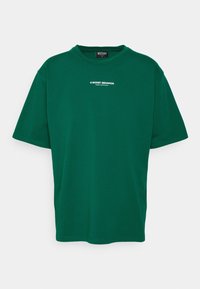 Grön kortärmad T-shirt i bomull med rund halsringning. Har vit text "© WORST BEHAVIOR" i mitten på framsidan.