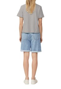 Gestreiftes kurzärmliges Oberteil in Creme und Marineblau, kombiniert mit hellblauen Denim-Shorts mit umgeschlagenen Säumen und zwei Gesäßtaschen. Weiße Sneakers.