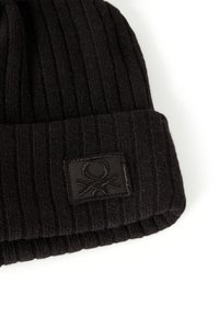 Černá žebrovaná čepice vyrobená z měkké látky, se skládacím lemem ozdobeným texturovaným černým logem.
