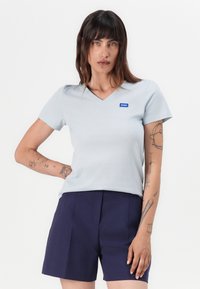 Ljust blå v-ringad t-shirt med korta ärmar, med en liten blå "HUGO"-logotyp, kombinerad med mörkblå shorts. Slät tygyta.