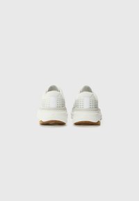 Zapatillas deportivas blancas con parte superior de malla texturizada, líneas laterales sutiles y suela de goma. Presenta un talón reforzado y un diseño minimalista.
