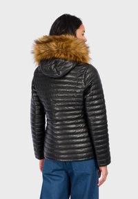 Černá bundu s kapucí, která má hnědý umělý kožešinový lem. Bunda má prošívaný design a přiléhavý střih.