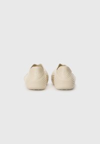 Bottines beiges à enfiler avec des nervures texturées sur le dessus, arrière arrondi et un design minimaliste. Présente un petit logo près du talon.