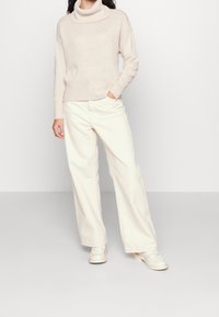 Vaaleanbeige neulefleece, jossa on ribbireuna, yhdistetty löysyihin kermaisiin housuihin ja valkoisiin slip-on-kenkiin.