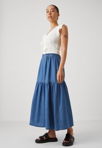 Bela bluzica iz broderie anglaise z ruffle rokavi, v kombinaciji z dolgo modro denim krilo in črnimi natikači. Minimalističen dizajn, brez vzorcev.