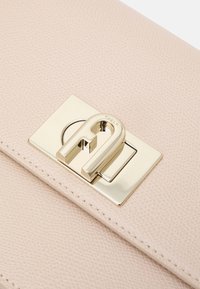 Borsa in pelle testurizzata rosa chiaro con chiusura a gancetto in metallo dorato dal design distintivo. I bordi cuciti completano l'aspetto raffinato.