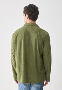 Green corduroy shirt with long sleeves, a collar, and textured vertical stripes, paired with blue jeans. Visible stitching details.