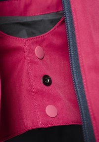 Interno di giacca magenta con texture a spina di pesce, dotato di un bottone a pressione nero e bottoni decorativi rosa vicino all'apertura con zip.