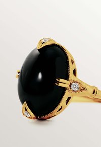 Anillo de oro con una gran piedra negra, acentuado con pequeños diamantes a cada lado, con un diseño intrincado en la banda, acabado suave y pulido.