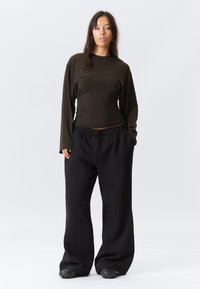 Maglietta a maniche lunghe di colore verde oliva scuro con design aderente, abbinata a pantaloni tuta neri larghi con vita elastica.