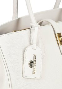 Witte handtas van textuurleer met twee handvaten, gouden hardware en een afneembare tag met de in reliëf aangebrachte tekst "WITTCHEN".