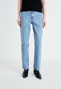 Light blue straight-leg jeans made of denim with a classic five-pocket design. Worn with black ankle boots featuring square toes.