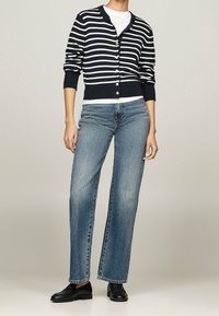 Cardigan a righe navy e bianche con bottoni, abbinato a jeans a gamba larga azzurri e mocassini neri. Design semplice e casual.