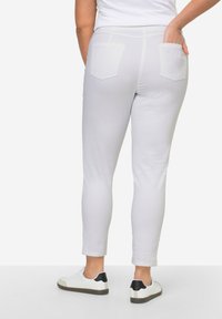 Harmaat housut, slim fit -muotoilu, valmistettu puuvillasekoitteesta, jossa on kaksi takataskua ja sileä pinta. Yhdistetty valkoisiin lenkkareihin.