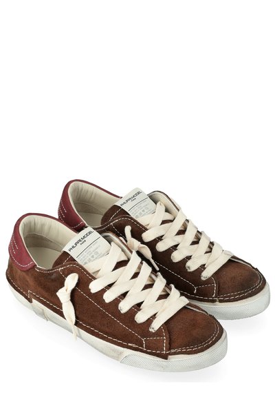 Sneaker in suede marrone con lacci beige e suola bianca, caratterizzati da un accento di tacco bordeaux e dettagli cuciti lungo i bordi.