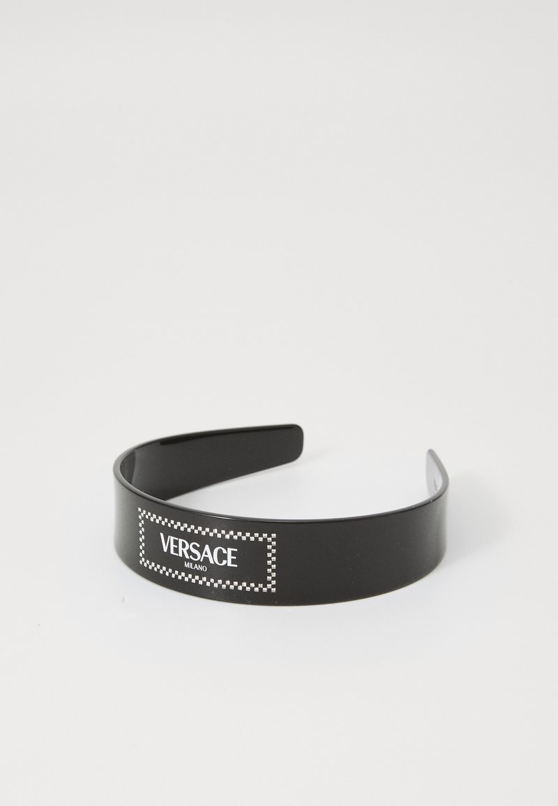 Juodas plastikinis plaukų juostelė su baltu stačiakampiu logo, kuriame yra užrašai "VERSACE" ir "MILANO", apraizgytas šaškėmis.