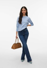 Pull-over bleu clair, silhouette ajustée, assorti à un jean évasé en denim foncé. Tient un sac à main en cuir marron clair, porte des talons pointus bleu clair.