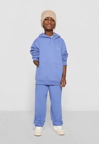 Light blue hoodie with a front pocket and matching sweatpants, paired with a beige knitted hat. Casual fabric and relaxed fit.