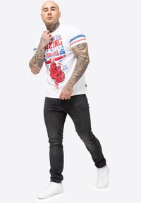 Balta trumpa rankovė t-shirt marškiniai su raudonu ir mėlynu bokso grafikos spaudiniu; derinami su juodomis džinsinėmis kelnėmis ir baltais sportbačiais. Paprastas, kasdieniškas dizainas.