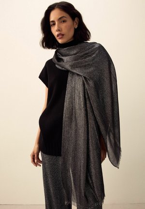 Schwarzer gestrickter Pullover mit kurzen Ärmeln, kombiniert mit einem schimmernden grauen Schal mit fransigen Rändern, elegant drapiert. Strukturiertes Gewebe.