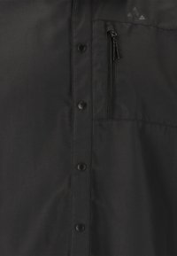 Zwarte jack met een ritszak op de borst, drukknoopsluiting en een gladde, lichtgewicht stof met een subtiele textuur.