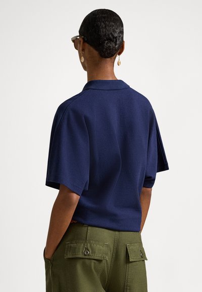 Σκούρο μπλε πουκάμισο με κοντά μανίκια και γιακά, με υφή υφάσματος και άνετη εφαρμογή, σε συνδυασμό με ελιάς πράσινο cargo παντελόνι.