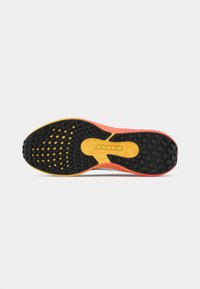 Suela de zapato con una plataforma de goma texturizada negra, acentos en naranja y amarillo, presentando un patrón de panal y detalles de marca.