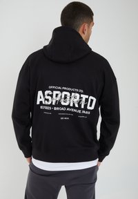 Sudadera negra con un gran texto gráfico blanco en la parte posterior, que presenta detalles de la marca. Fabricada con un tejido suave, tiene un ajuste holgado y capucha con cordón.
