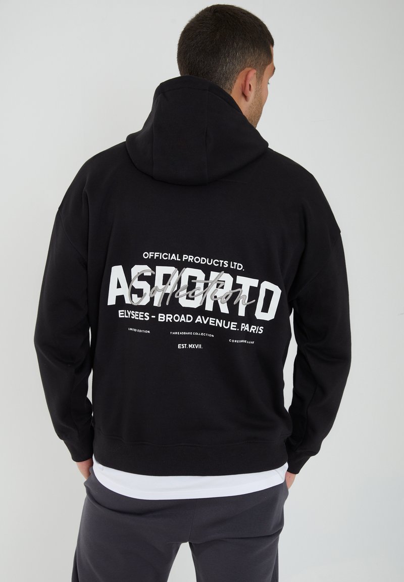 Sudadera negra con un gran texto gráfico blanco en la parte posterior, que presenta detalles de la marca. Fabricada con un tejido suave, tiene un ajuste holgado y capucha con cordón.