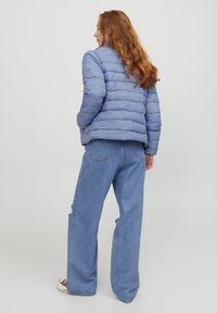 Giacca a vento azzurra chiara con design trapuntato, abbinata a jeans blu a vita alta e dal taglio morbido. Tessuto soffice e vestibilità rilassata.