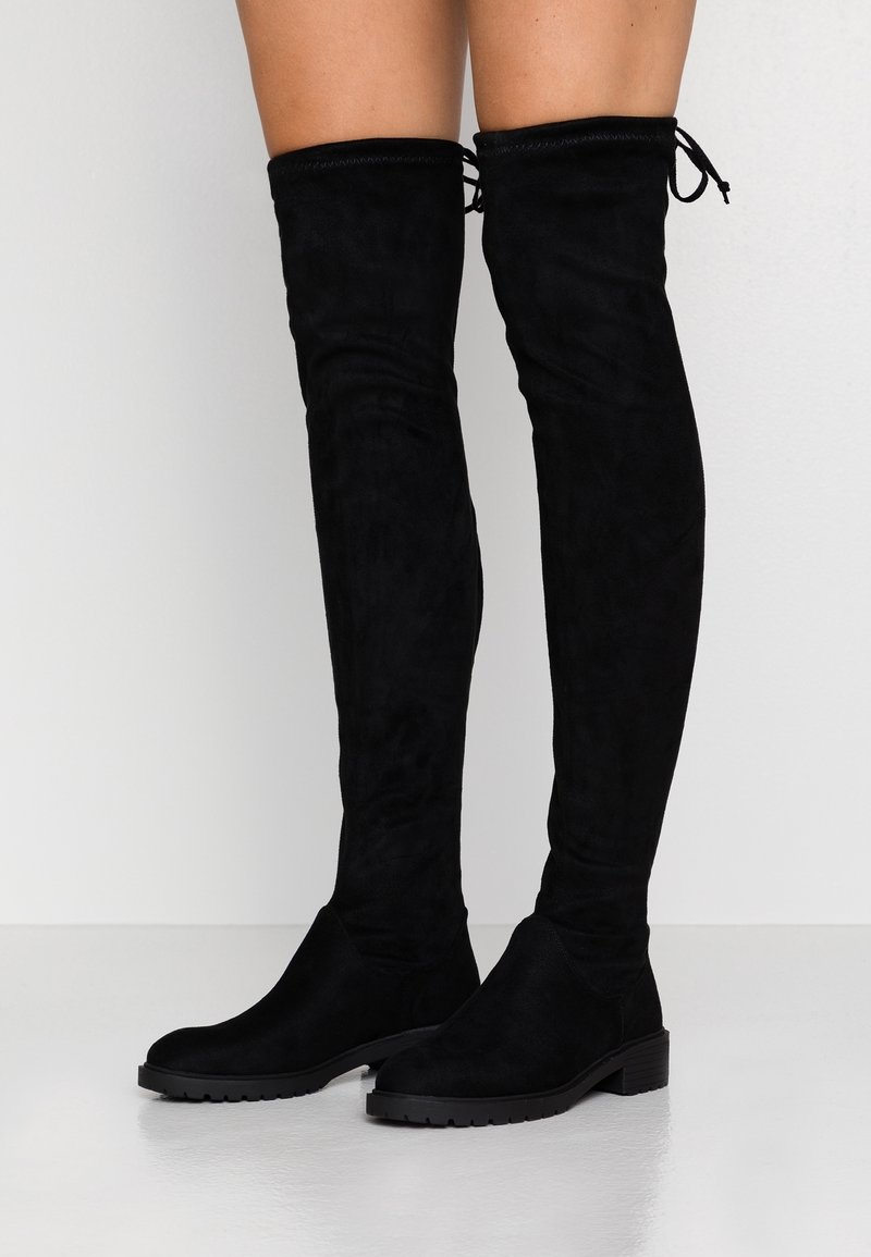 Bottes cuissardes en daim noir avec bout arrondi, finition texturée et cordon ajustable en haut. Semelle en caoutchouc noire robuste.