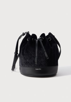 Sac seau noir Calvin Klein à cordon de serrage, avec un corps en tissu matelassé, une base en cuir, des œillets en métal et une bandoulière réglable.