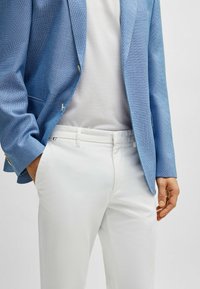 Ljust blå strukturerad blazer med två knappar, kombinerad med en vit åtsittande skjorta och skräddarsydda vita byxor. Anmärkningsvärd sidoficka på byxorna.