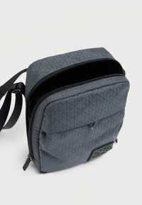 Γκρι υφασμάτινη τσάντα χιαστί με φερμουάρ, διαμάντι σχέδιο, μπροστινή τσέπη και ρυθμιζόμενο λουράκι. Υφασμάτινη λογότυπο μπατζάκι μπροστά.