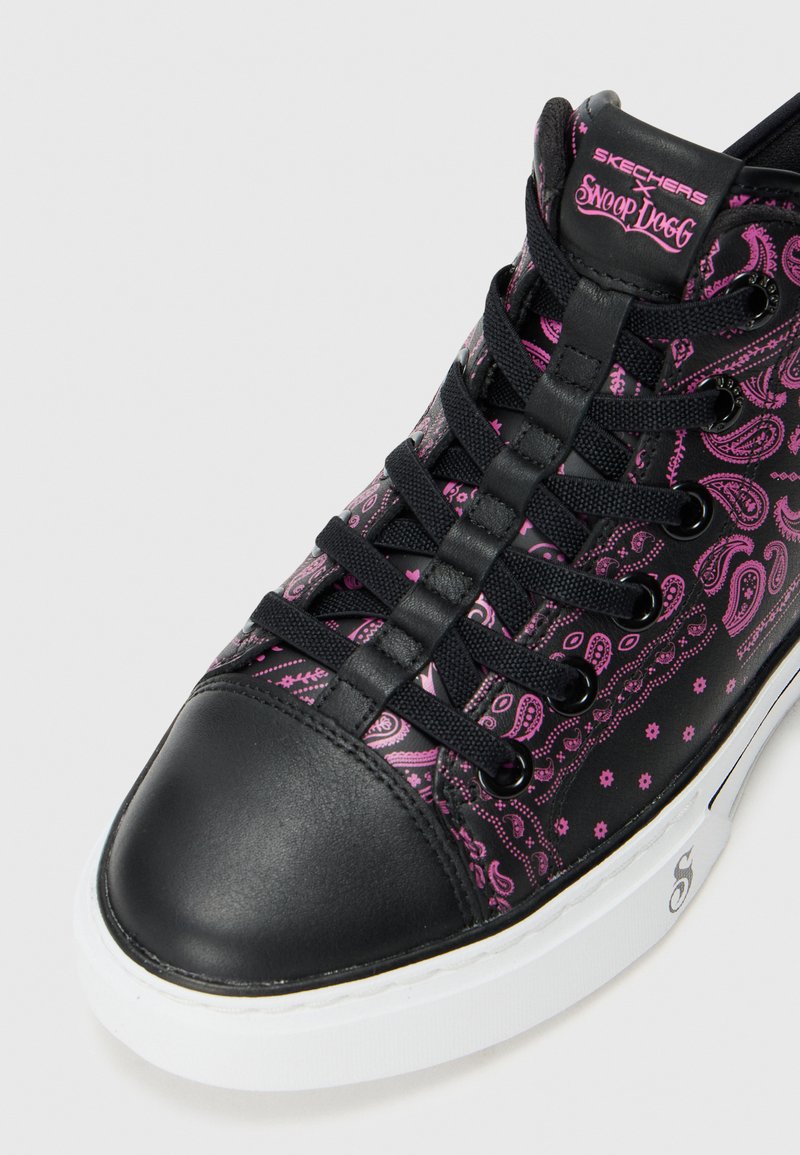 Sneaker Skechers con punta in pelle nera e motivo paisley rosa su tessuto nero, con lacci neri e suola bianca.