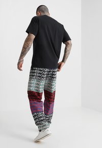 Schwarzes Baumwoll-T-Shirt kombiniert mit bunten, gemusterten Jogginghosen mit Text. Die Materialien sind weich; die Hosen haben einen elastischen Bund und Bündchen.