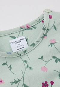 Vihreä puuvillapaita, jossa on kukkakuvaus, jossa on vaaleanpunaisia ja sinisiä kukkia. Pyöreä pääntie, jossa on nappikiinnitys. Merkkilogo näkyvissä.