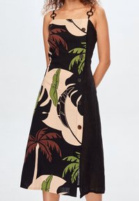 Abito nero e beige con motivi a foglie di palma, taglio asimmetrico, design dei manici con accenti circolari e bottoni marroni lungo il lato.