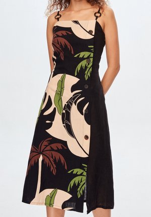 Schwarz-beiges Kleid mit Palmblattmustern, asymmetrischem Schnitt, Trägerdesign mit runden Akzenten und braunen Knöpfen an der Seite.