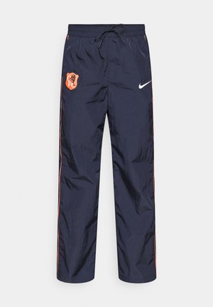 Pantaloni de tip windbreaker bleumarin, cu textură lucioasă, având un patch portocaliu cu logo și dungi laterale. Talie elastică cu șnur de strângere.