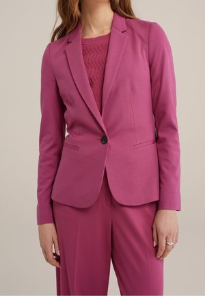 Vrouw draagt een op maat gemaakte donkerroze blazer met een enkele zwarte knoop, bijpassende brede broekspijpen en daaronder een gestructureerde gebreide top.