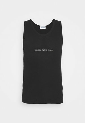 Musta farkkutakki etutaskuilla, jota on päällä mustan tanktopin kanssa, yhdistettynä tummansinisiin farkkuihin ja mustiin nauhakenkiin.