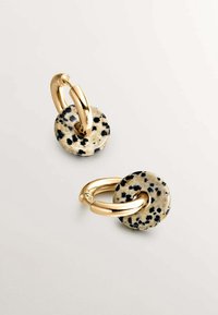 Pendientes de aro en tono dorado con piedras circulares de jaspe dálmata, que presentan un patrón moteado en negro y beige. Acabados metálicos lisos.