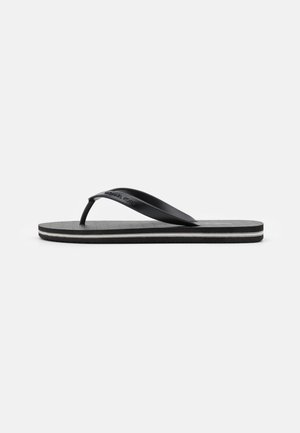 Schwarze Flip-Flop-Sandale mit strukturiertem Fußbett, dünnen Riemen und einem weißen Akzentstreifen an der Sohle. Aus flexiblem Gummimaterial gefertigt.