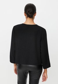 Zwarte, gestructureerde, boxy trui met lange mouwen en een ronde hals, gecombineerd met nauwsluitende zwarte broek.