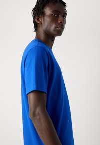 Camiseta de algodón azul con mangas cortas, cuello redondo y un diseño liso. La tela parece suave con un ligero brillo. Se muestra la vista lateral.