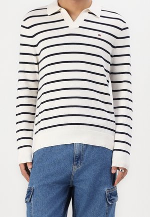 White long-sleeve polo sweater with black horizontal stripes worn with blue cargo jeans, showing torso and upper legs.